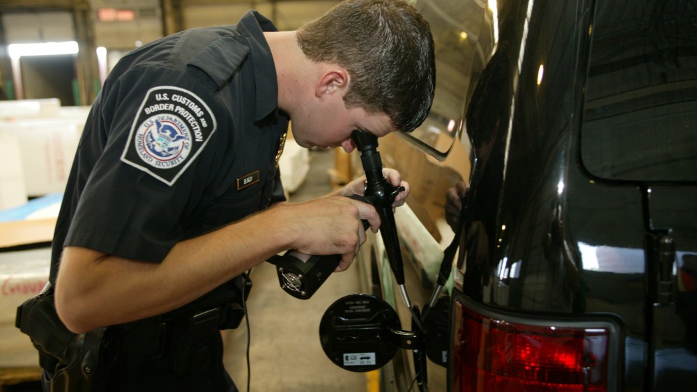 A CBP officer inspects a shipment using a magnifying instrument. The vehicle is transporting imports.