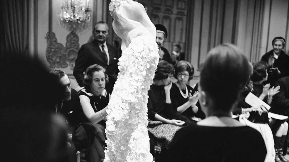 Buyers examine the fabric of a floor-length bridal gown with floral appliqué, veil and headpiece from the James Galanos Couture Spring 1964 collection.