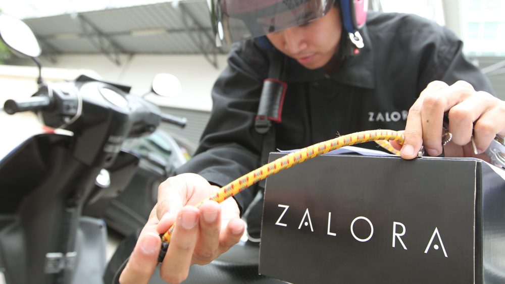 A Zalora delivery driver secures a package to his moped.