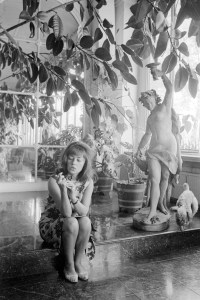 Outtake; Portrait of French actress Jeanne Moreau wearing a loose chemisey dress of orange silk with black scroll print and no make-up during an interview with Women's Wear Daily, accompanied by a bouncing blue-fox color, small sized poodle named Voyou (gutter-snipe) in Paris, France, circa August 1964.Article title: "La Moreau"