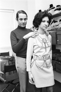 American costume jewelry designer Kenneth Jay Lane draping a necklace and belt of his design on a model, 1968.