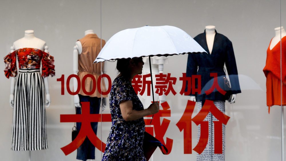 A woman carries an umbrella past a fashion outlet offering its summer sale at a shopping mall in Beijing.