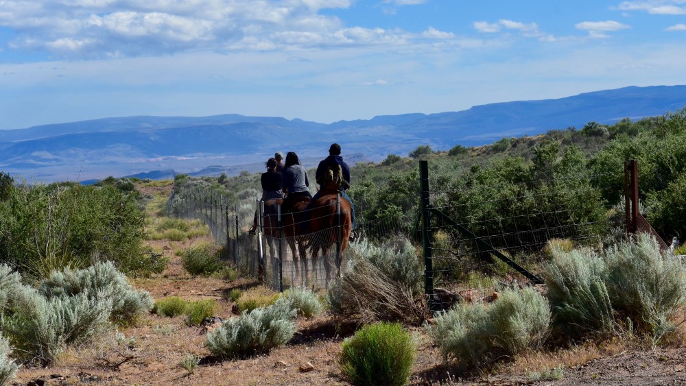 Back view of people on horseback traveling through the southwest landscape of sage and mountains in distance.; Shutterstock ID 636839164; Usage: web; Issue Date: 8/8/17