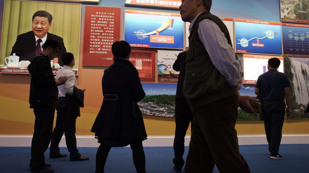 Visitors walk past a chart showing China's soaring GDP since 2012 and a photo of Chinese President Xi Jinping.