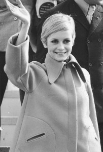 Outtake; Twiggy wearing a turquoise velour romper and turquoise tights (with a run high on the inside left thigh) under a orange fleece tent coat with her boyfriend Justin De Villeneuve attending a press conference for their arrival from London at the Kennedy International Airport on March 20, 1967 in New York...Article title: "The Fashions: The World's Narrowest Girl"