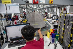 An employee puts various parts of jewerly in a tray onto a conveyor belt where it will be taken off and completed at different work stations.