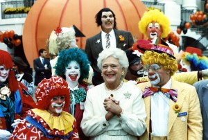 First Lady Barbara Bush grinning as she poses with costumed performers, a group of clowns, and a lone werewolf on the South Grounds of the White House as part of a Halloween celebration.