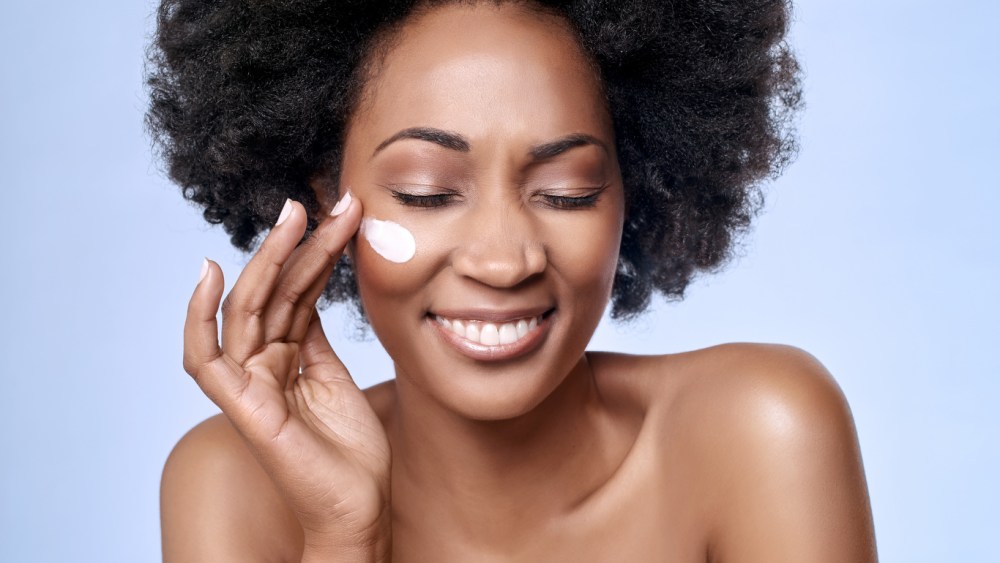 Beautiful black african model with flawless skin smooth complexion applying moisturiser face cream to her cheek, beauty cosmetics skincare concept; Shutterstock ID 324717266; Usage (Print, Web, Both): both; Issue Date: 2 oct; Comments: wwd
