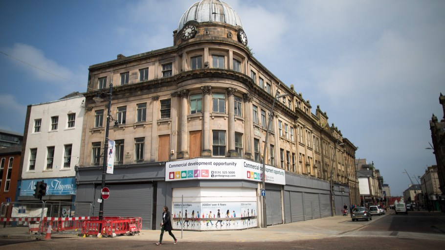 A pedestrian walks past shuttered shops on a high street in Sunderland, U.K.