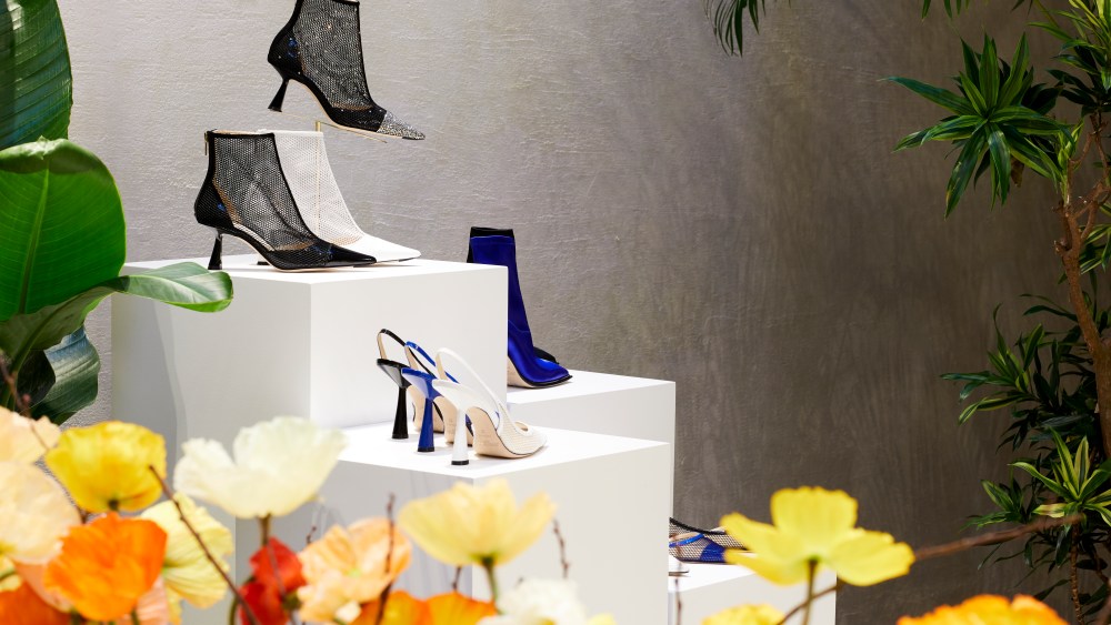 A stack of mesh Jimmy Choo Pre-Fall 2019 heels amid a border of orange and yellow flowers.