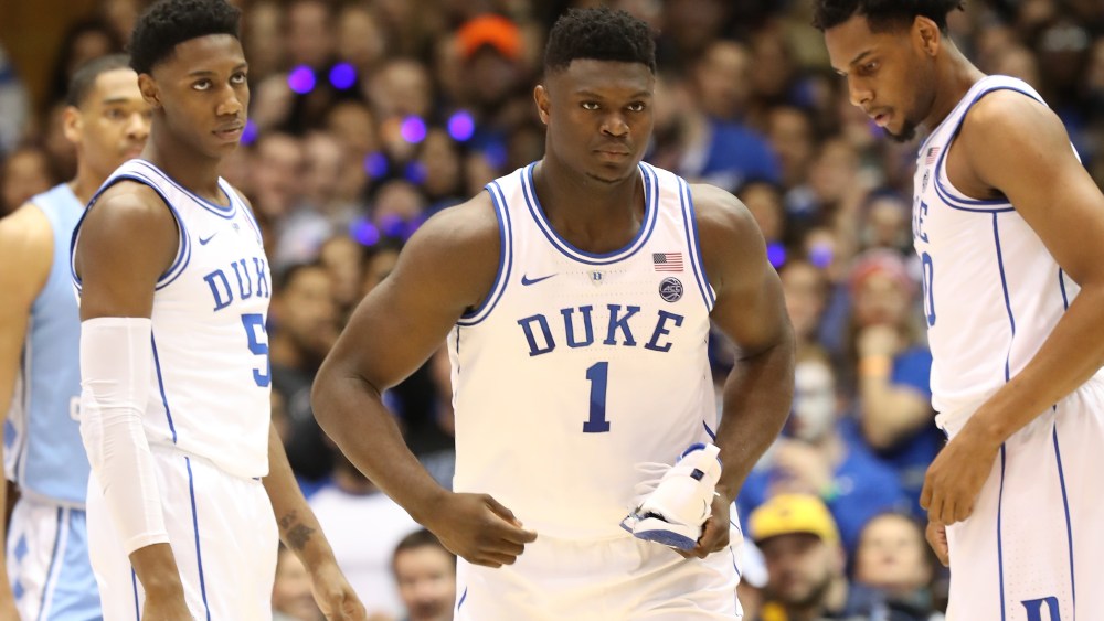 Teammates RJ Barrett #5 and Marques Bolden #20 of the Duke Blue Devils watch as Zion Williamson #1 of the Duke Blue Devils reacts after falling as his shoe breaks against Luke Maye #32 of the North Carolina Tar Heels during their game at Cameron Indoor Stadium on February 20, 2019 in Durham, North Carolina.