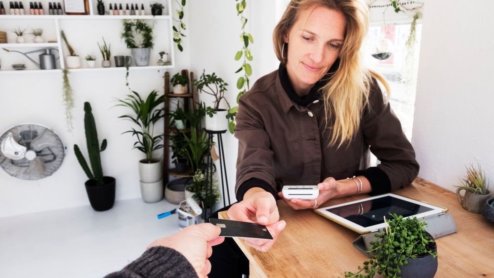 MODEL RELEASED Female owner of plant shop receiving credit card from customer for payment of small String of Pearls plant in black pot.VARIOUS