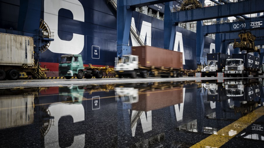 Trucks are reflected in a puddle as they wait in line to unload their containers onto CMA CGM SA's Benjamin Franklin container ship docked at the Guangzhou Nansha Container Port in Guangzhou, China.