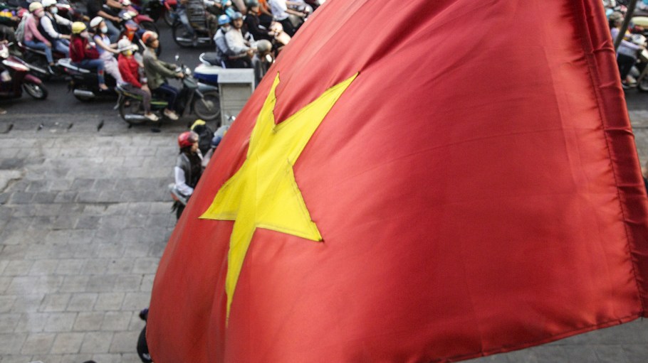 A Vietnamese national flag flies as motorcyclists wait at a traffic signal in Ho Chi Minh City, Vietnam, on Friday, Jan. 12, 2018.