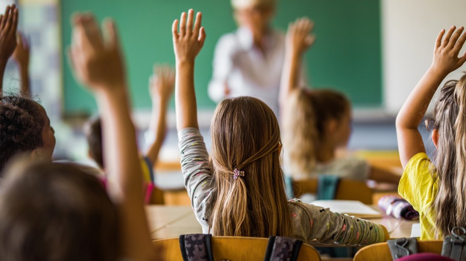 children sitting in a classroom raising their hands