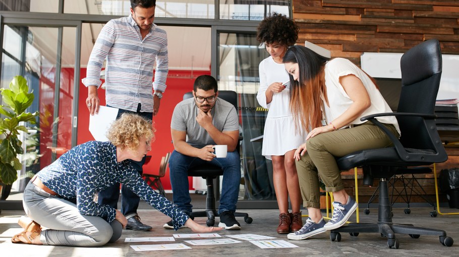 Creative people looking at project plan laid out on floor. Mixed race business associates discussing new project plan in modern office.