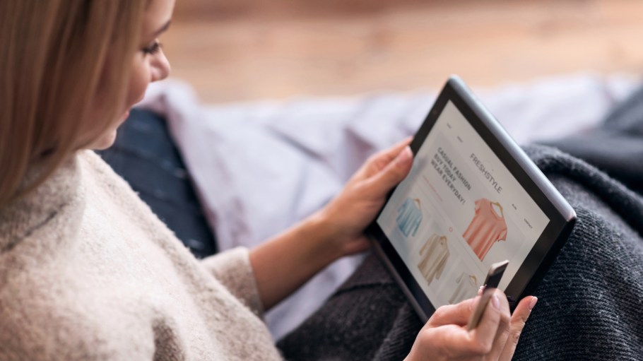 Joyful young pretty woman enjoying online shopping and using tablet and credit card while sitting in bed.