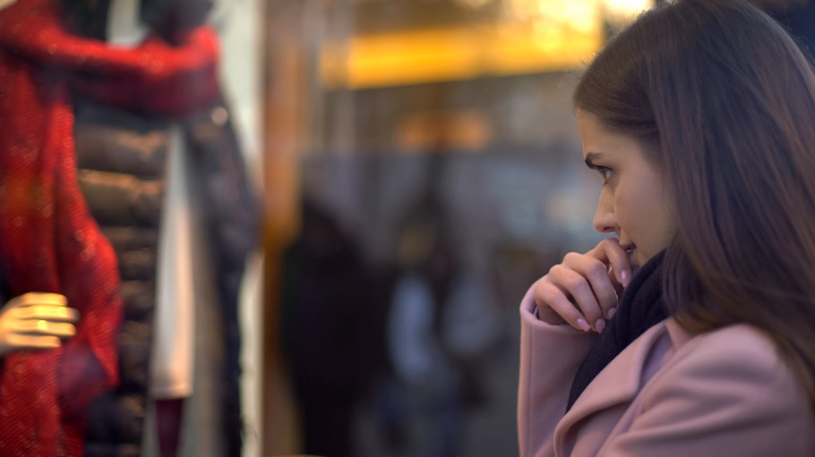 Beautiful lady looking at clothing in shop window, having not enough money