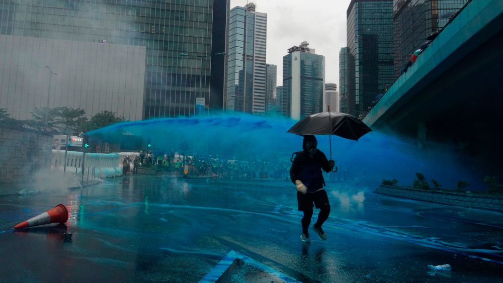 A protestor runs for cover as police fire blue-colored water from water cannons in Hong Kong.