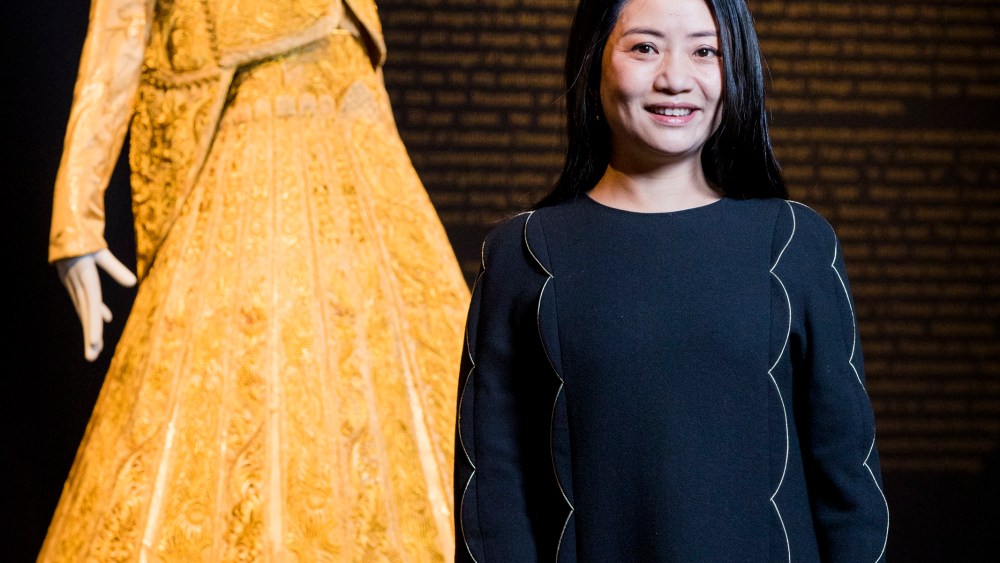 Guo Pei, stands alongside her gold traditional bridal dress at Sotheby's