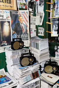 The installation includes a recreated newsstand with iconic newspaper headlines plastering the wall.