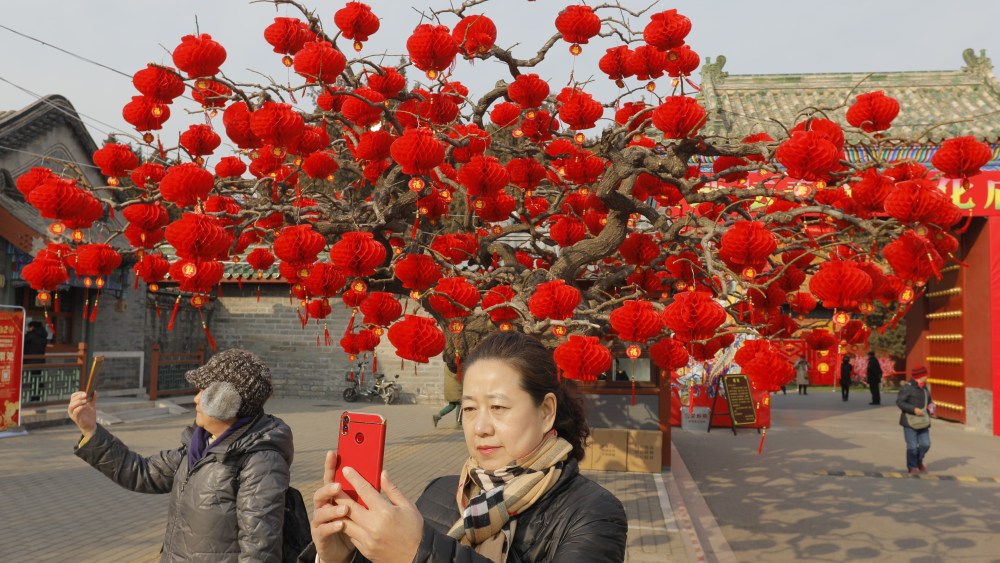 People take photos near a tree decorated with red lanterns ahead of the upcoming Chinese Lunar New Year at Ditan Park in Beijing, China.