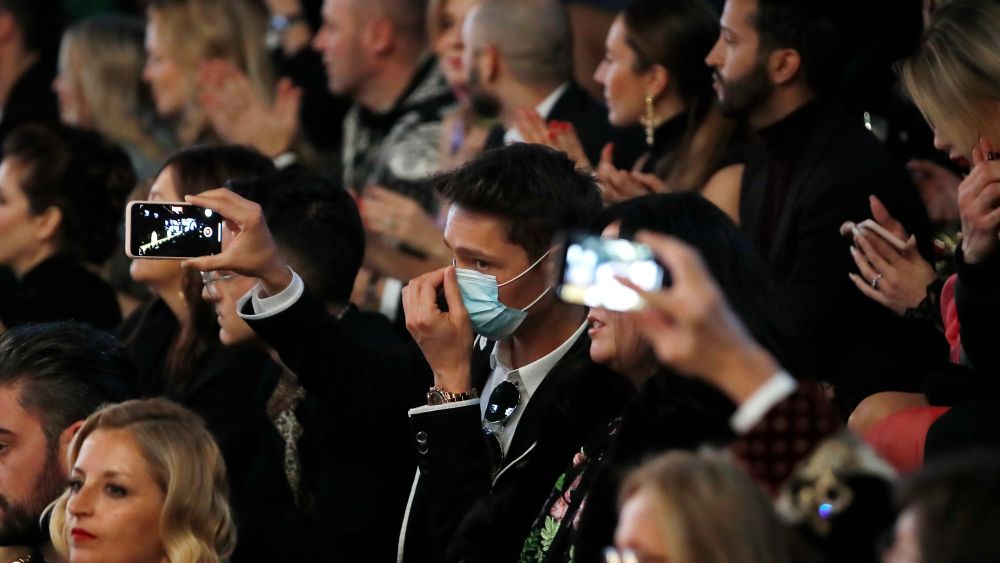 A man wearing a sanitary mask takes photos during the Dolce & Gabbana women's Fall Winter 2020-21 show, in Milan, Italy, . After Giorgio Armani's last-minute decision to show his latest collection in an empty theater due to concerns about the new virus, the rest of Milan's runway shows scheduled for Sunday are to go ahead as planned, fashion officials confirmedFashion F/W 20/21 Dolce & Gabbana, Milan, Italy - 23 Feb 2020