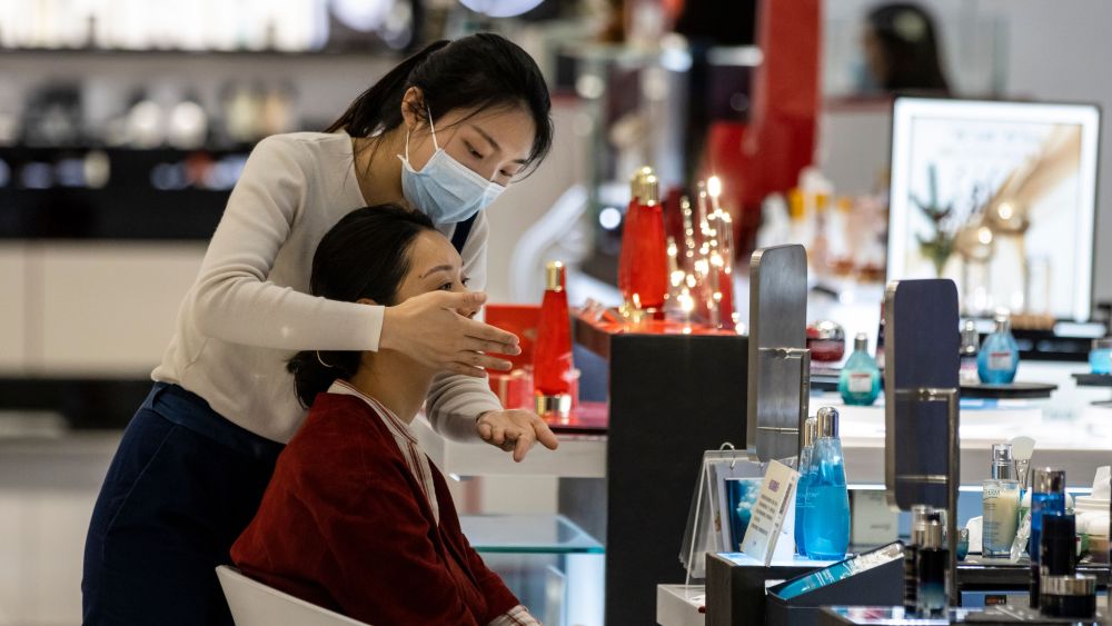 A woman wears a mask as she works in shopping mall cosmetic department in Guangzhou.