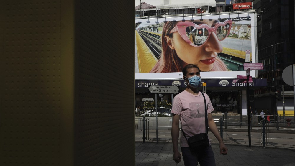 A mask-wearing pedestrian walks past an advertising billboard in Tsim Sha Tsui, Hong Kong.