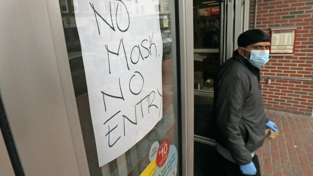 Masked shopper walks past a sign taped to the front door of a CVS Pharmacy, requesting patrons wear masks if they intend on shopping inside due to the COVID-19 virus outbreak, in Chelsea, MassVirus Outbreak Masssachusetts, Chelsea, United States - 28 Apr 2020