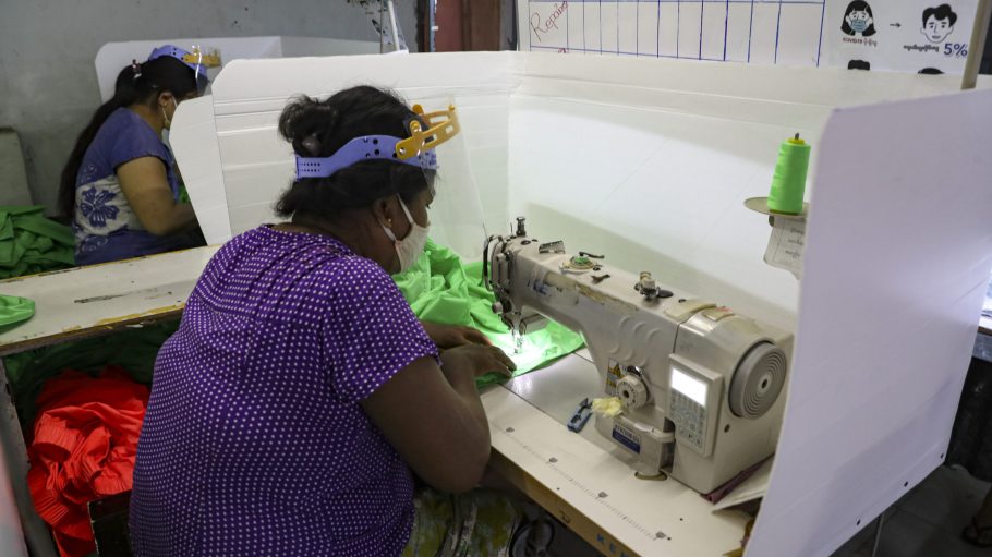 Workers wearing face mask and face shield to help curb the spread of the new coronavirus, sew behind white partition surrounding their sewing tables as they work at a garment factory, at Industrial Zone in Yangon, Myanmar