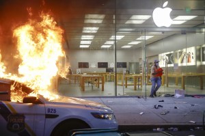Protester leaves the Apple Store as a police car burns in Philadelphia.