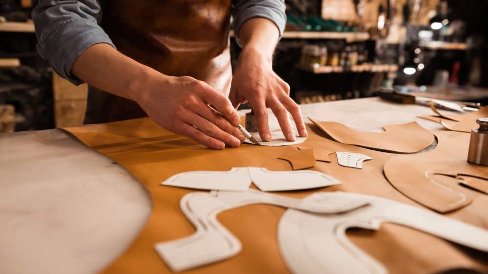Close up of a shoemaker measuring and cutting leather in a workshop