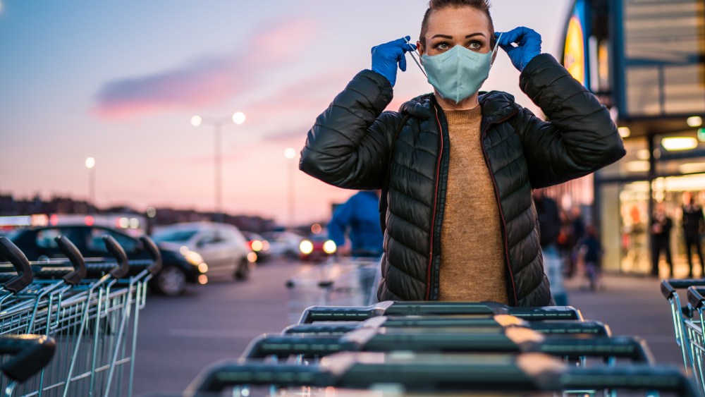 Woman with protective gloves puts a medical mask on her face as a virus protection in a supermarket parking lot.