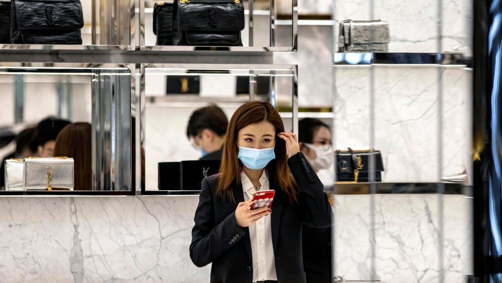 A woman wearing a protective face mask stands at Yves Saint Laurent shop in Guangzhou.
