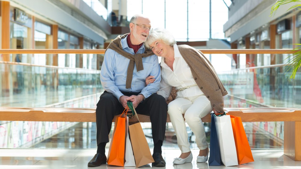 Senior couple sitting in shopping mall with gifts
