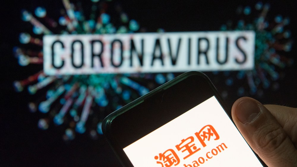ATaobao logo displayed on a smartphone with a computer model of the COVID-19 coronavirus on the background.