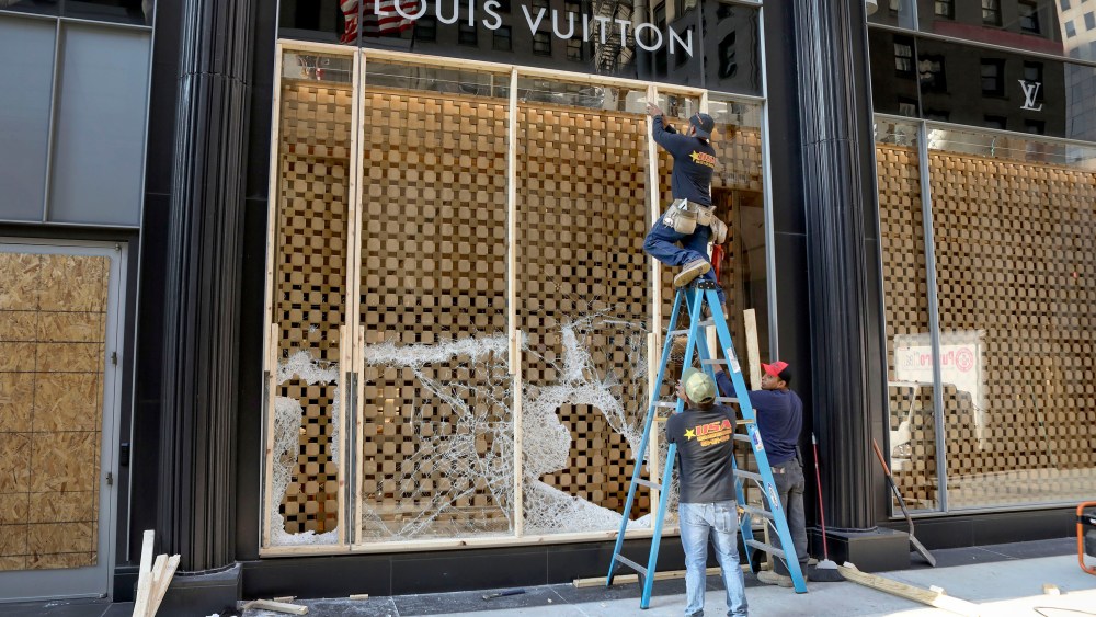 Workers begin to board up a display window at the Louis Vuitton store Monday, Aug. 10, 2020, after overnight vandals hit many high-end stores in Chicago. Chicago's police commissioner says more than 100 people were arrested following a night of looting and unrest that left several officers injured and caused damage in the city's upscale Magnificent Mile shopping district and other parts of the city. (AP Photo/Teresa Crawford)
