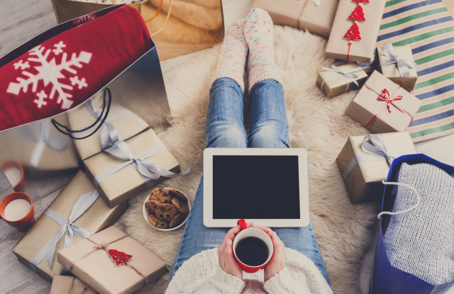 Christmas online shopping top view. Female buyer touch screen of tablet, copy space. Woman has coffee, buys presents, prepare to xmas eve, sitting among gifts boxes and packages. Winter holidays sales