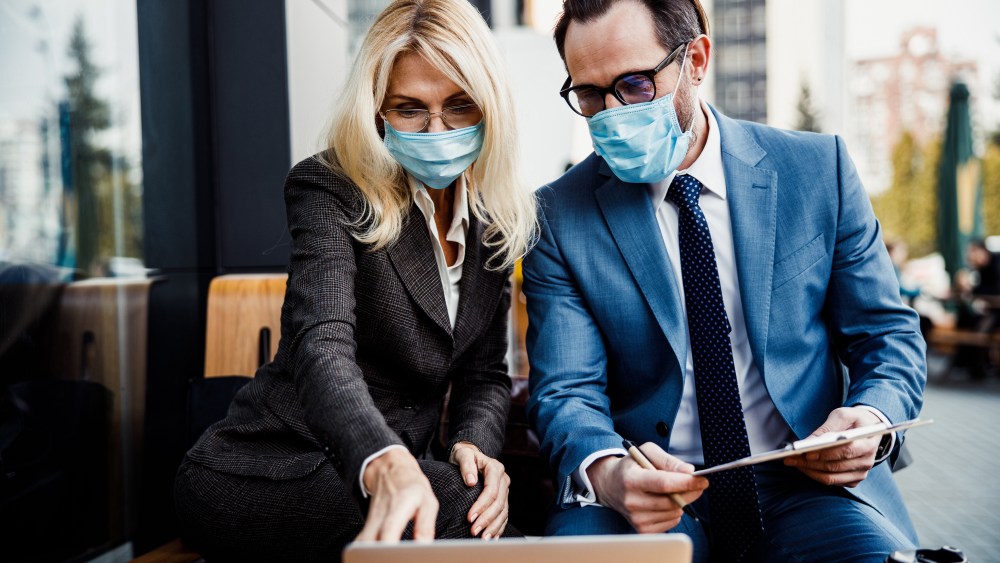 Front view of two people in eyeglasses and protective masks sitting in a street cafe
