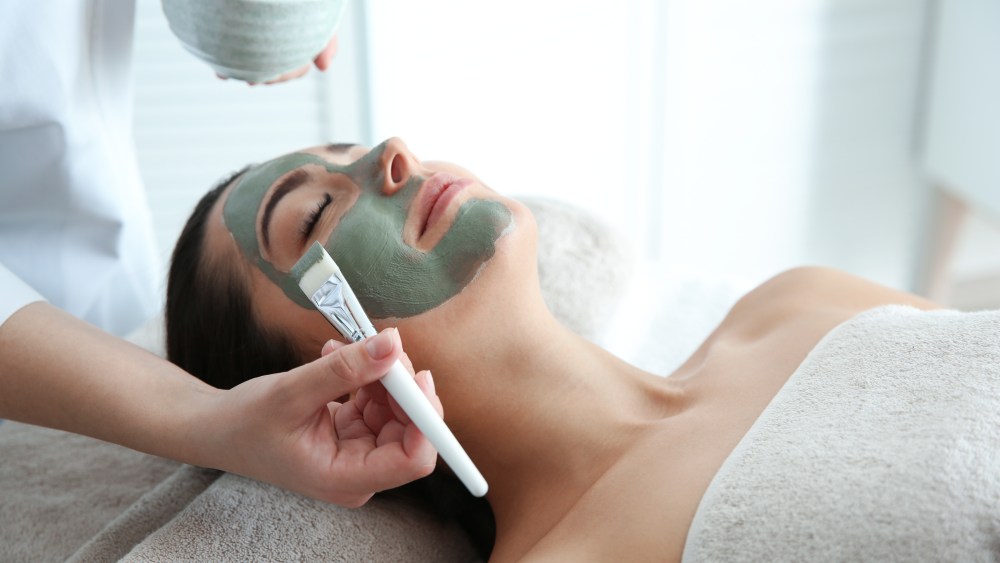 Cosmetologist applying mask on client's face in spa salon