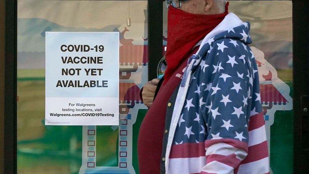 A pedestrian wearing a mask walks past a sign advising that COVID-19 vaccines are not available yet at a Walgreen's pharmacy store during the coronavirus outbreak in San Francisco, Wednesday, Dec. 2, 2020. (AP Photo/Jeff Chiu)