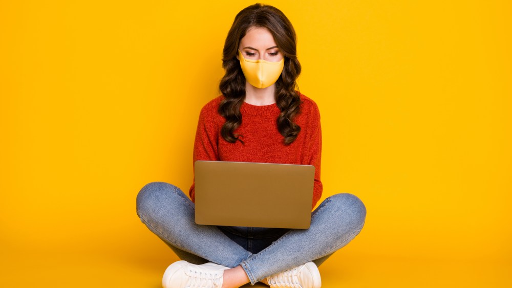 women in mask sitting typing laptop