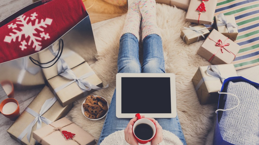 Christmas online shopping top view. Female buyer touch screen of tablet, copy space. Woman has coffee, buys presents, prepare to xmas eve, sitting among gifts boxes and packages. Winter holidays sales