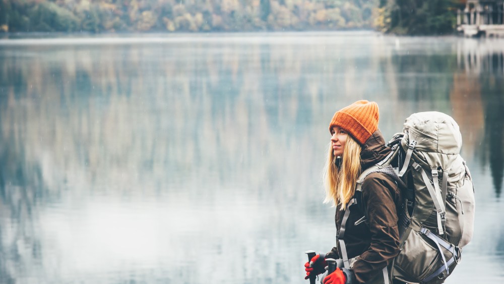 Woman with backpack hiking Lifestyle adventure concept forest and lake on background active vacations into the wild