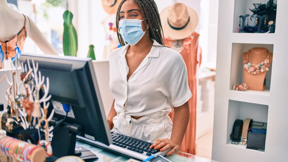 clothing store sales associate in mask at cash register