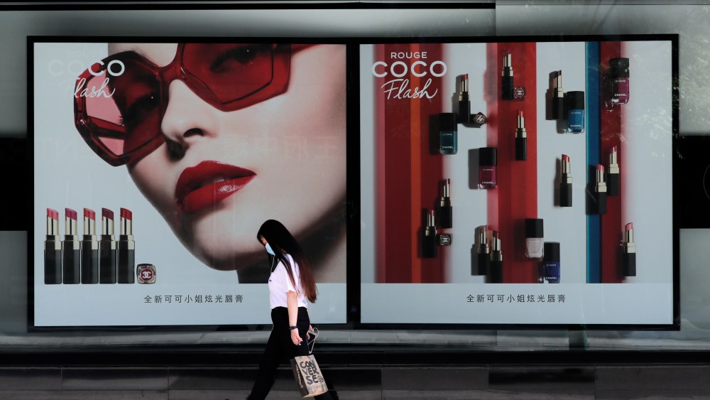 FILE - IN this Thursday, May 28, 2020 file photo, a woman wearing a protective face mask to help curb the spread of coronavirus walks past a Chanel lipstick advertisement billboard in Beijing. Sales of luxury apparel, jewelry and beauty products are set to slide by nearly a quarter this year as the pandemic wipes out more than six years of growth, according to a study released Wednesday, Nov. 18, 2020 by the consultancy Bain.  (AP Photo/Andy Wong, File)