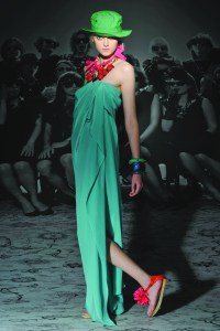 Fashion shot of a model at a presentation for the 2010 Cruise/Resort ready-to-wear (rtw) show for Lanvin designed by Alber Elbaz, wearing a long strapless aqua blue gown with pink flat sandals, several bracelets, a green soft hat and an oversize necklace in pink