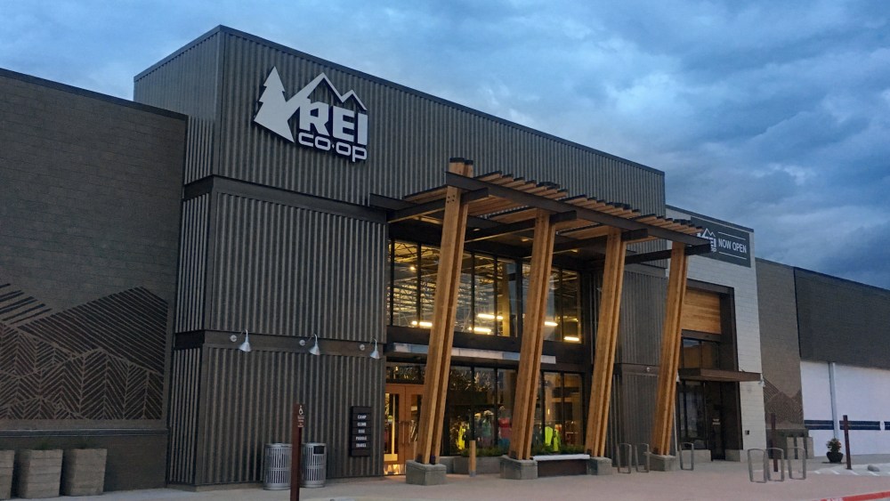 An REI storefront in Fort Worth, Texas shot against a cloudy sky.