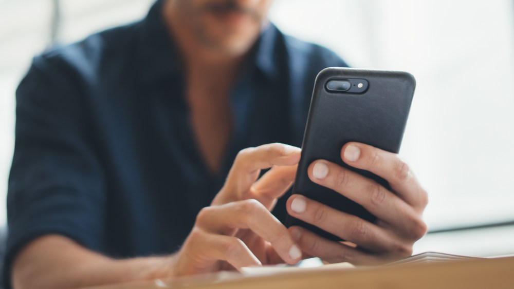 Close up photo of male hands with smartphone. Frreelancer at home office